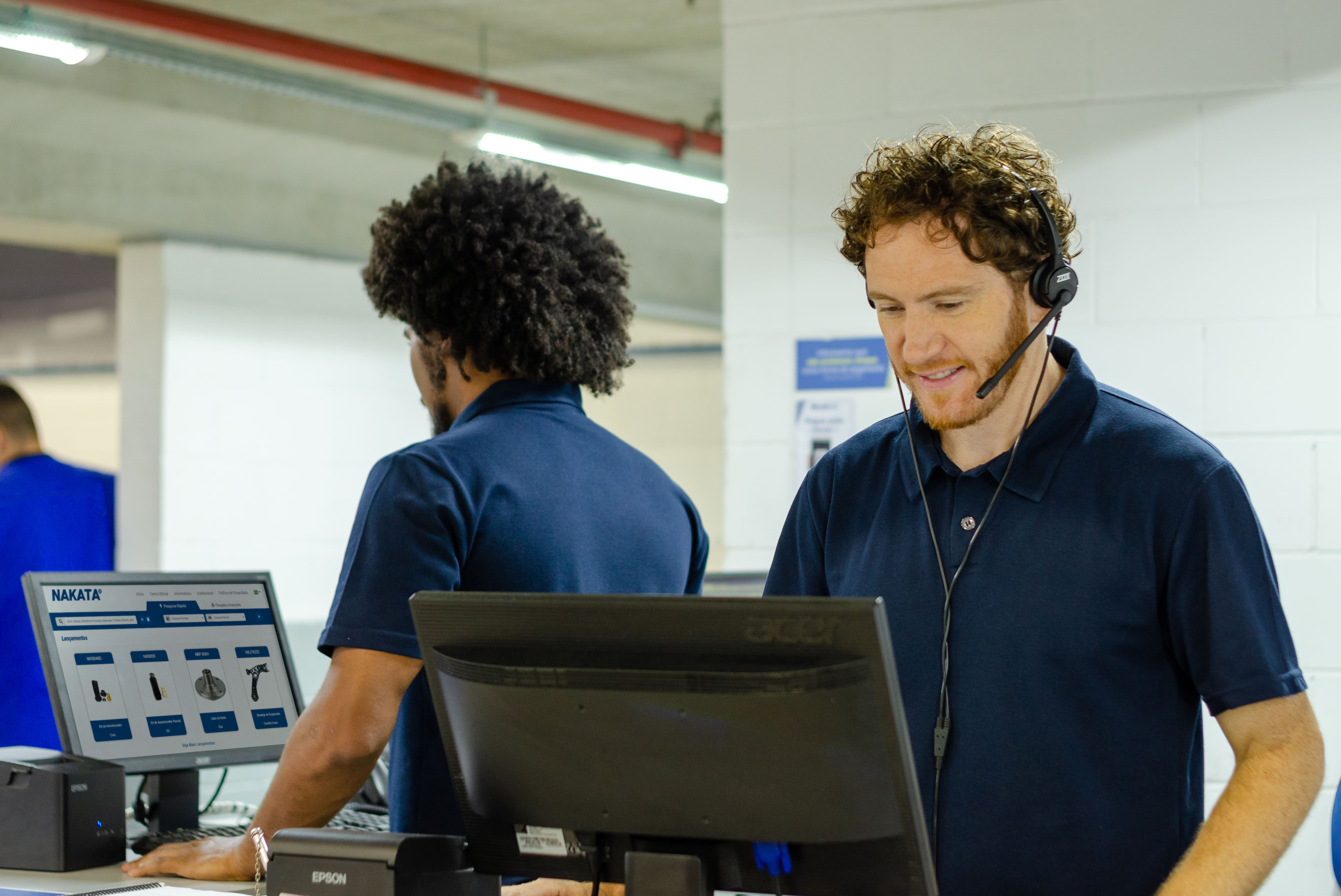 Imagem mostra vendedores usando computadores durante o atendimento no balcão de autopeças