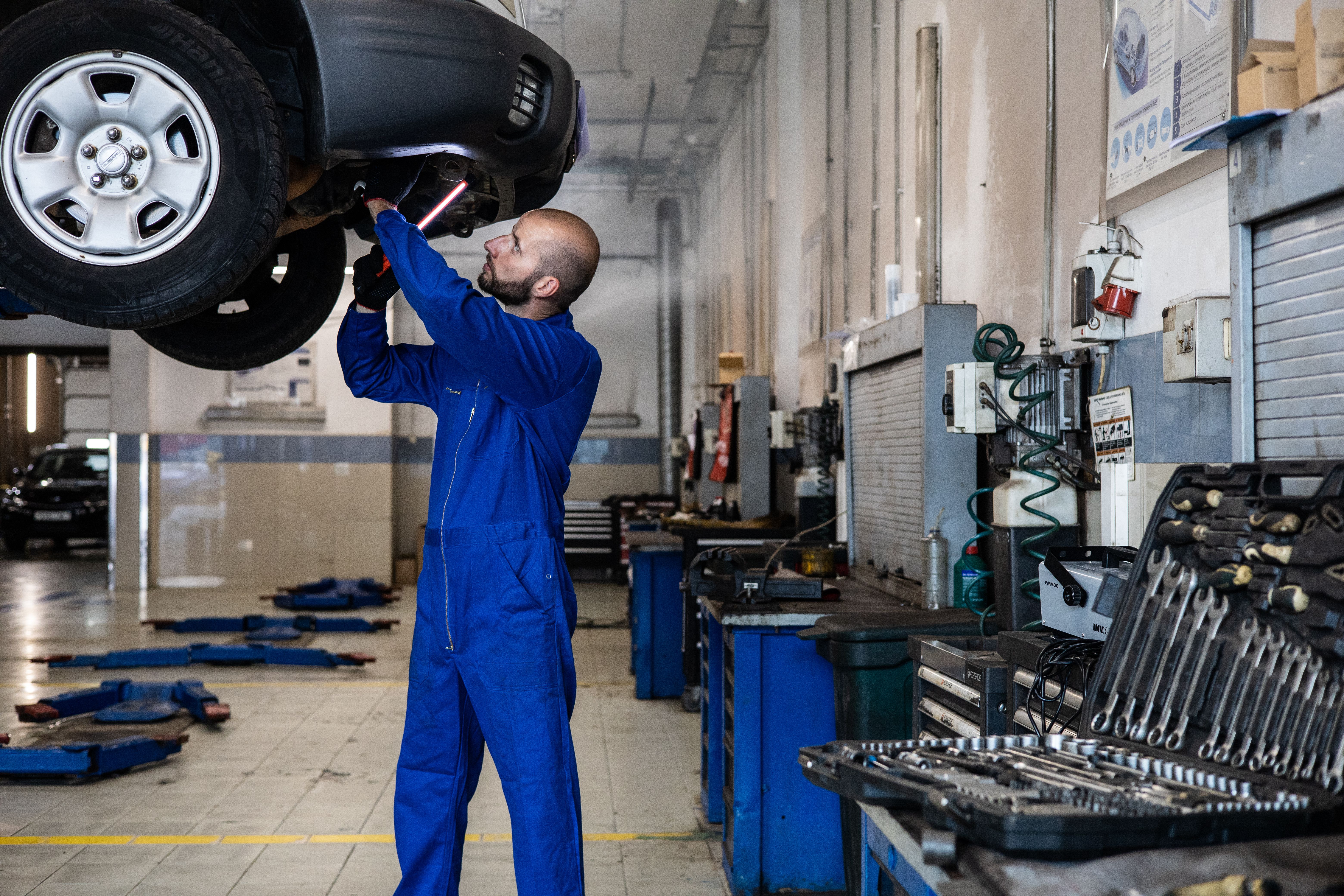 Imagem mostra mecânico inspecionando um carro elevado em uma oficina automotiva