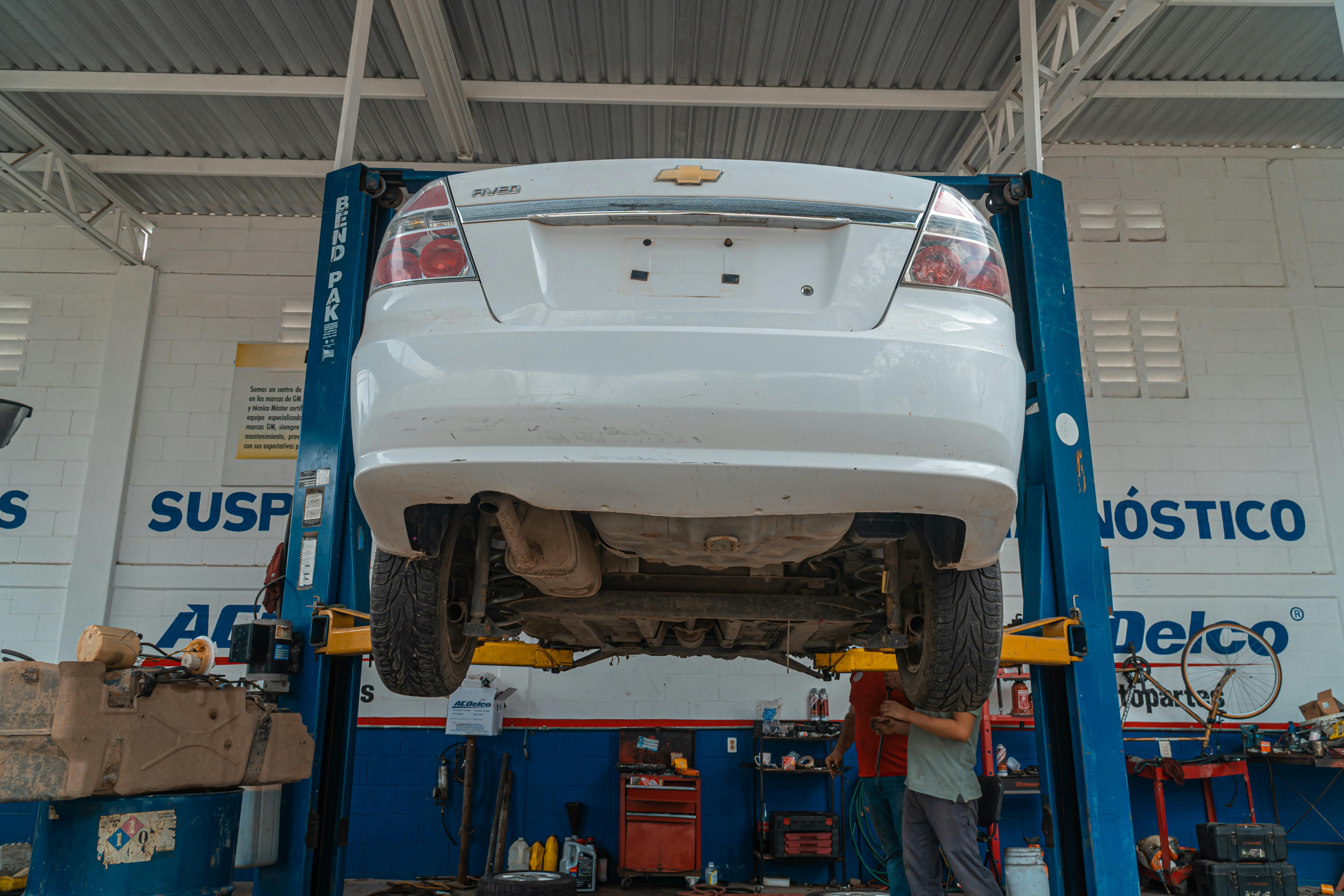  Imagem mostra carro branco elevado em oficina mecânica durante manutenção 