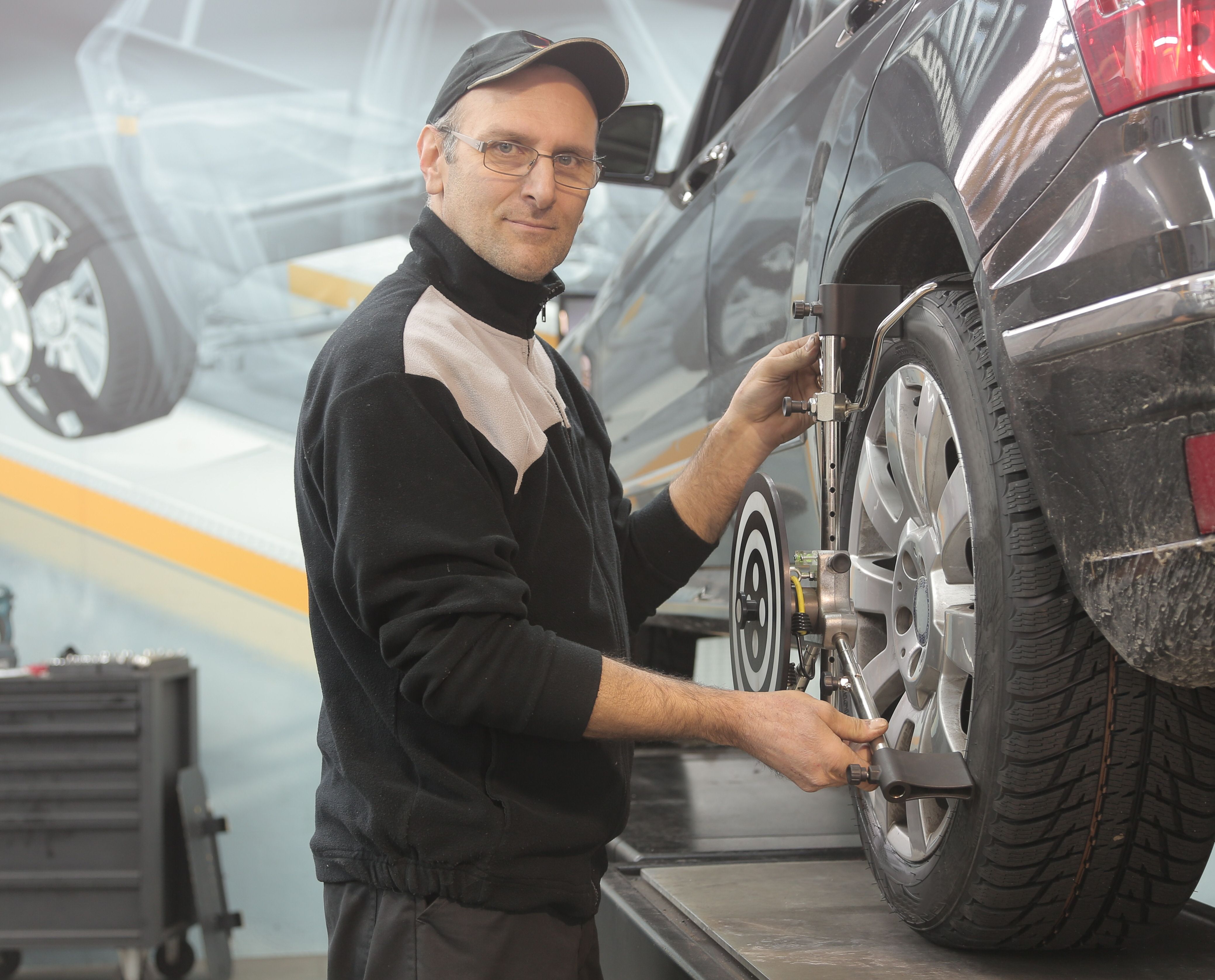 Imagem mostra mecânico ajustando equipamento de alinhamento na roda de um carro dentro de uma oficina