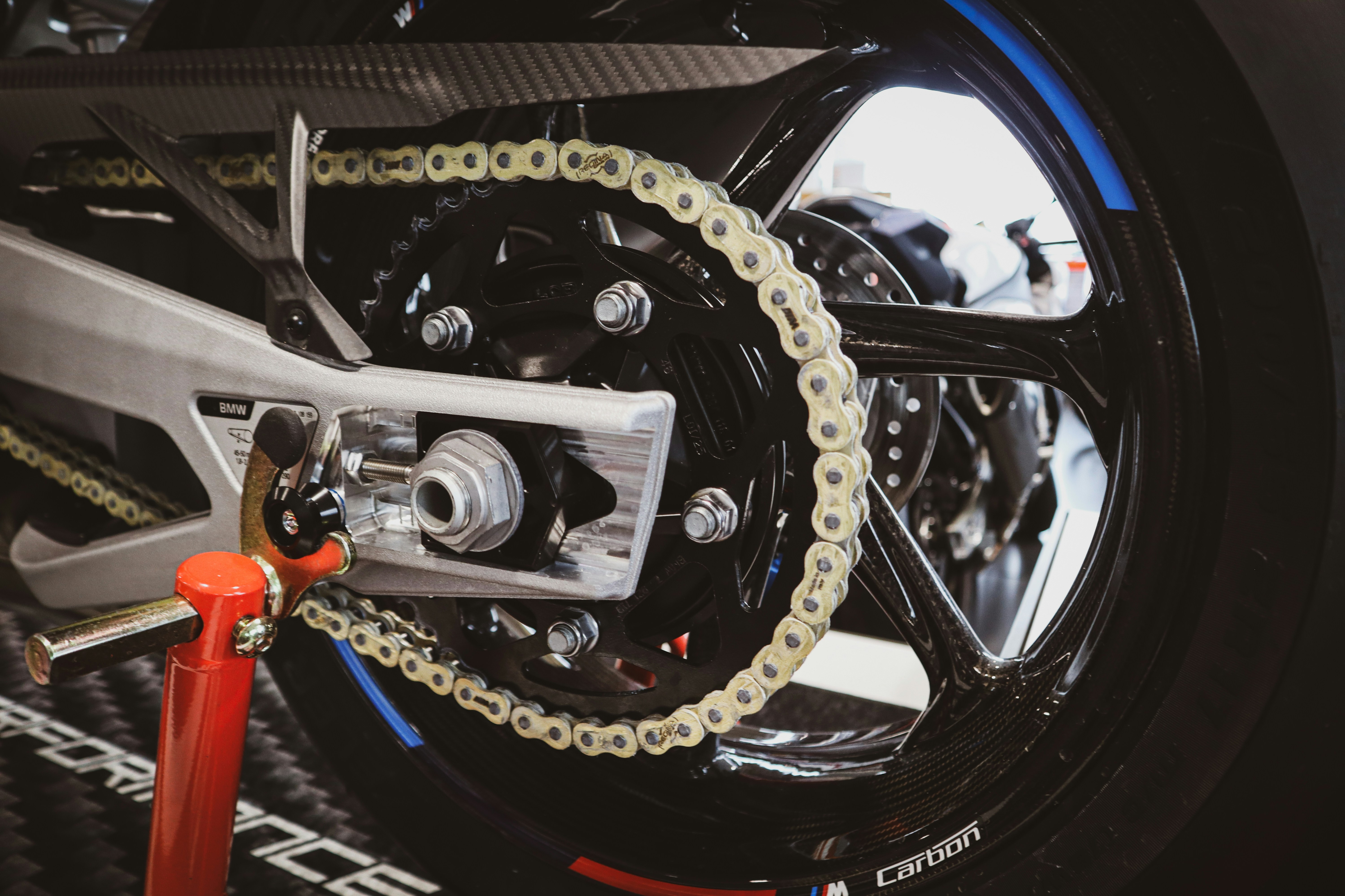 Imagem em close da roda traseira, da corrente e da coroa de uma motocicleta, destacando componentes ligados à transmissão.