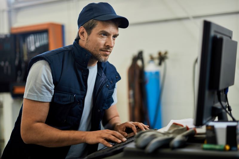 Imagem mostra profissional automotivo usando computador para consultar informações durante a rotina de trabalho